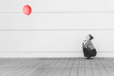 Woman looking at balloon while crouching on footpath - UUF22066