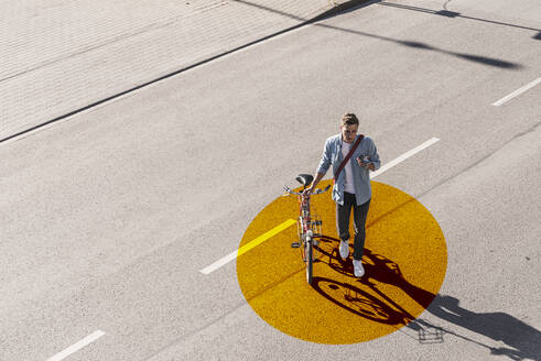 Mann mit Fahrrad, der ein Mobiltelefon benutzt, während er auf einer Straße mit goldfarbenem Kreis geht - UUF22068