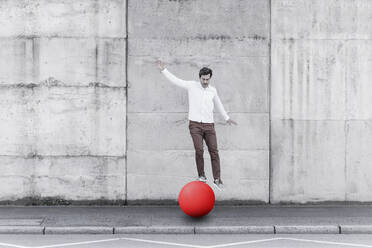Man balancing on fitness ball against wall - UUF22071
