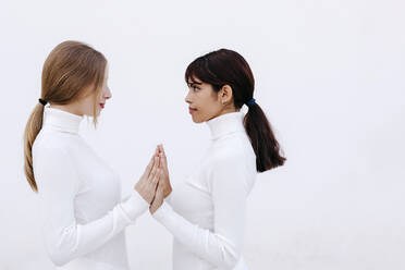 Young women touching hands while looking at each other against white background - TCEF01296