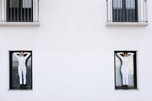 Junge Frauen stehen an den Fenstern eines weißen Gebäudes und schreien, während sie sich die Ohren zuhalten, während COVID-19 - TCEF01301