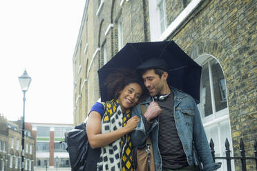Lächelnde Frau, die sich beim Spaziergang in der Stadt an einen Mann mit Regenschirm lehnt - AJOF00611