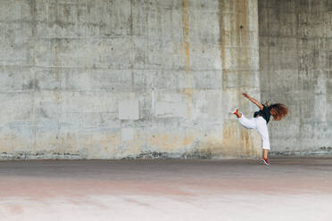 Junge Frau macht akrobatische Sprünge, während sie an der Wand trainiert - ABAYF00021