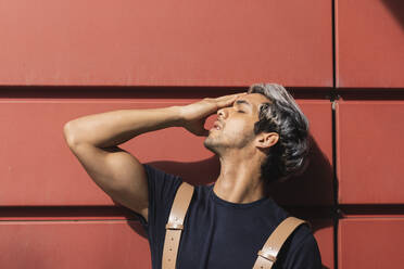 Young man with eyes closed standing against red wall - PNAF00153