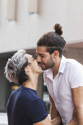 Lächelndes schwules Paar küsst sich vor einem Gebäude in der Stadt - PNAF00174
