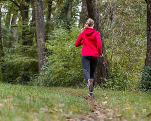 Junge Sportlerin joggt auf einer Wiese im Wald - STSF02655