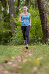 Active female athlete jogging in forest - STSF02656