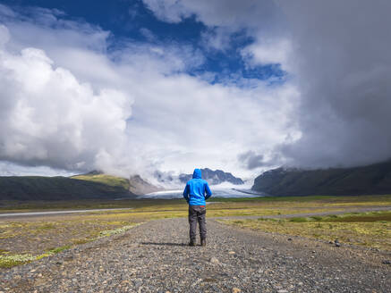 Mann auf unbefestigter Straße vor dramatischem Himmel am Svinafellsjokull, Island - LAF02513