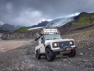Mann fährt Geländewagen gegen den bewölkten Himmel am Svinafellsjokull, Island - LAF02520