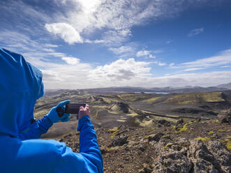 Mann fotografiert die Landschaft mit seinem Smartphone an einem sonnigen Tag, Lakagigar, Island - LAF02534