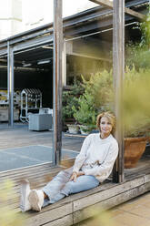 Thoughtful woman sitting on floor at rooftop garden - JRFF04925