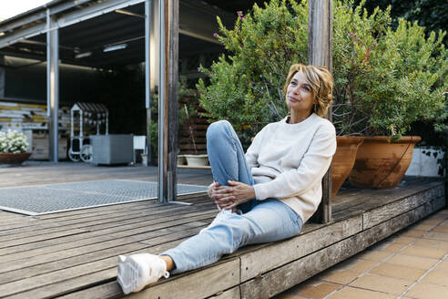 Nachdenkliche Frau, die auf einem Holzboden im Dachgarten sitzt - JRFF04926
