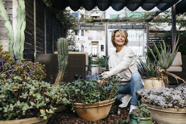 Smiling woman crouching by potted plant at rooftop garden - JRFF04927