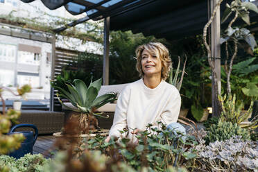 Smiling woman looking away amidst plant at rooftop garden - JRFF04929