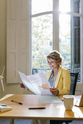 Smiling female engineer examining blueprint while sitting in office - JRFF04937