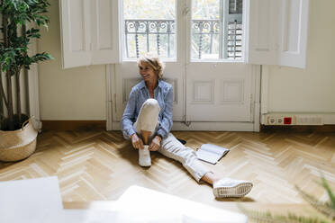 Smiling female entrepreneur sitting on floor against window in office - JRFF04956