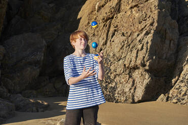 Boy juggling balls while playing at beach - JEDF00336