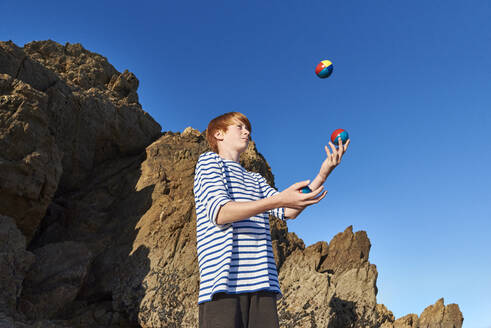 Boy juggling balls while playing against clear sky - JEDF00337
