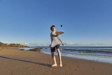 Junge spielt mit Ball und Schläger, während er am Strand steht - JEDF00341