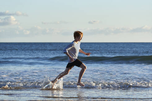Smiling boy running in water at beach - JEDF00343