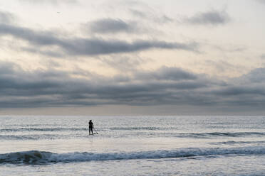 Woman paddleboarding on sea against sky during dawn - EGAF01030