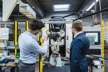 Geschäftsmann erklärt einem männlichen Kollegen die Maschinen in einer industriellen Fabrik - DIGF13115
