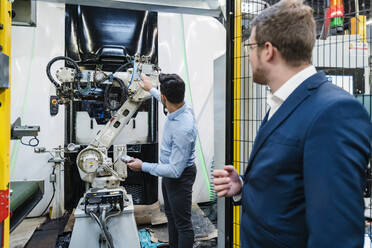 Mitarbeiter betrachten einen Roboterarm, während sie in einer Fabrik stehen - DIGF13116