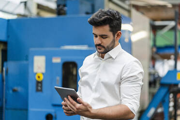 Männlicher Unternehmer, der ein digitales Tablet benutzt, während er in einer Fabrik steht - DIGF13136