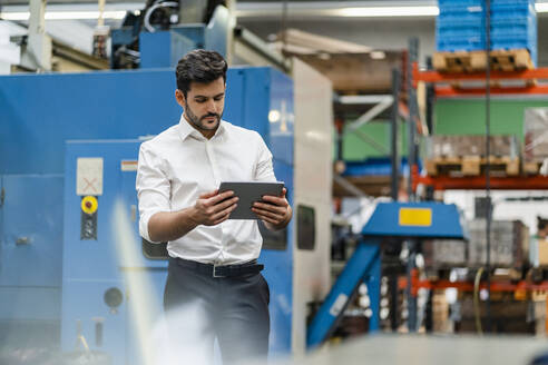 Geschäftsmann, der ein digitales Tablet benutzt, während er in einer Fabrik steht - DIGF13137