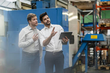 Male colleagues looking away while holding digital tablet while standing in manufacturing industry - DIGF13138