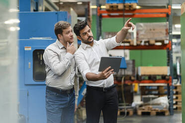 Male colleagues pointing while businessman standing beside him in manufacturing industry - DIGF13139