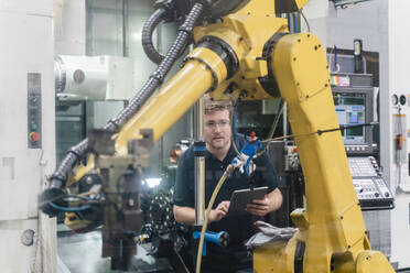 Male worker analyzing robotic arm while holding digital tablet in factory - DIGF13153