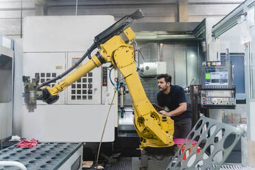 Young male worker analyzing robotic arm in manufacturing factory - DIGF13155