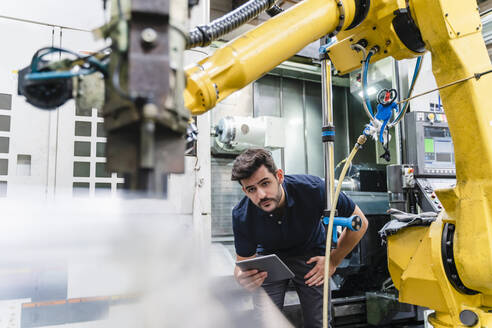 Männlicher Arbeiter mit digitalem Tablet, der einen Roboterarm in einer Fabrik untersucht - DIGF13156