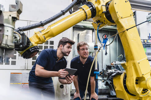 Männliche Mitarbeiter diskutieren über einen Roboterarm in einer Fabrik - DIGF13158