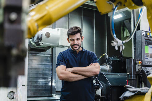 Male manual worker with arms crossed smiling while standing in factory - DIGF13164