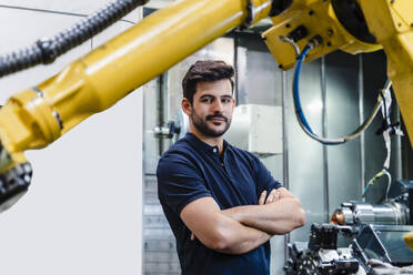 Selbstbewusster männlicher Arbeiter mit verschränkten Armen in einer Fabrik stehend - DIGF13165