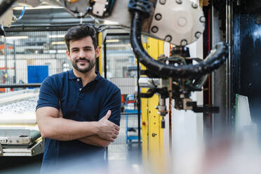 Lächelnder männlicher Arbeiter mit verschränkten Armen in der Industrie stehend - DIGF13222