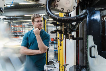 Nachdenklicher männlicher Arbeiter, der in einer Fabrik stehend untersucht - DIGF13223