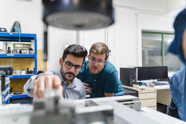 Businessman and male colleague examining surveyor machine in manufacturing factory - DIGF13232