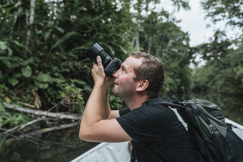 Männlicher Rucksacktourist fotografiert die Natur vom Kanu aus am Napo-Fluss, Ecuador - DSIF00195