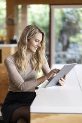 Junge Frau, die zu Hause sitzend an einem digitalen Tablet arbeitet - PESF02138