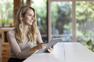 Frau mit digitalem Tablet, die wegschaut, während sie zu Hause sitzt - PESF02139