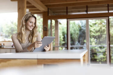 Woman smiling while working on digital tablet at home - PESF02140
