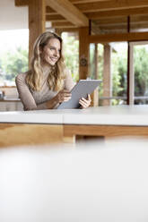 Junge Frau schaut weg, während sie ein digitales Tablet zu Hause benutzt - PESF02141