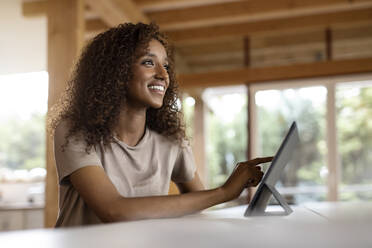 Lächelnde Geschäftsfrau, die ein digitales Tablet benutzt, während sie zu Hause am Tisch sitzt - PESF02159
