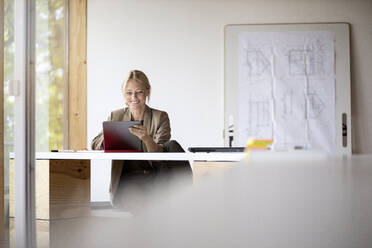 Businesswoman smiling while working on digital tablet at home - PESF02169