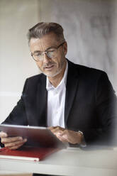 Geschäftsmann mit Brille, der bei der Arbeit zu Hause ein digitales Tablet benutzt - PESF02174