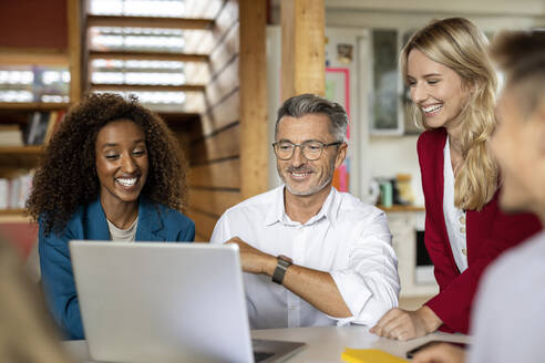 Lächelnde Geschäftsleute, die einen Laptop benutzen, während sie in einer Besprechung im Büro zusammenarbeiten - PESF02198