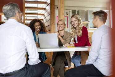 Geschäftsleute, die lächelnd in einer Sitzung zusammenarbeiten, während sie im Büro sitzen - PESF02199